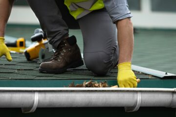 roof repairman removing dried leaves on gutter