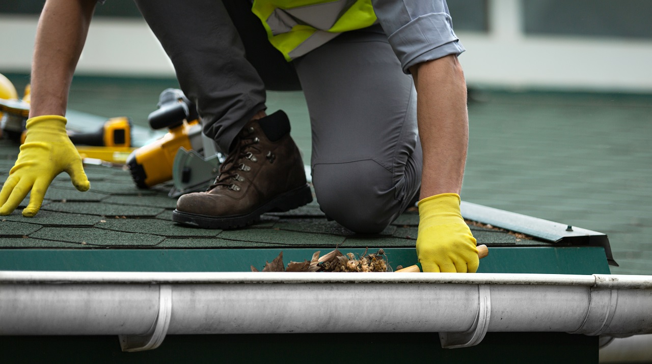 roof repairman removing dried leaves on gutter